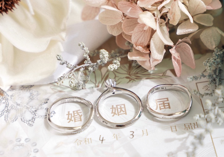 「婚姻届」の文字一つ一つにリングをのせてクローズアップ撮影。奥に白、淡いピンク、小花の花を添えて。
